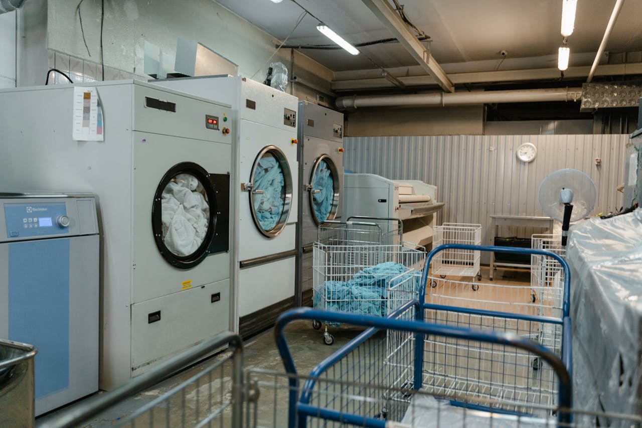 services-04 Interior view of an industrial laundry room with washers and rolling carts.