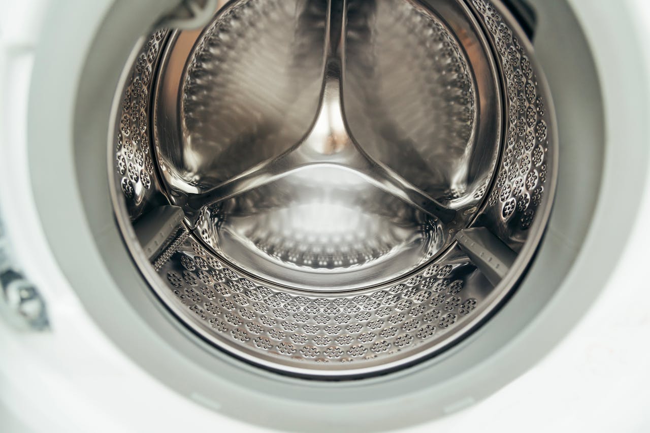 services-01 Detailed view of a clean, modern washing machine drum, showcasing shiny stainless steel interior.